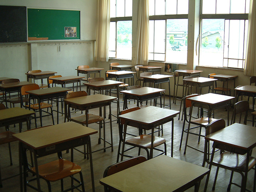 Pusta klasa z ławkami i białą tablicą, bez napisów na tablicy.